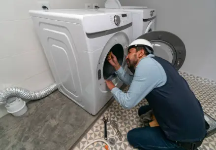 Technician repairing a laundry appliance next to its vent hose