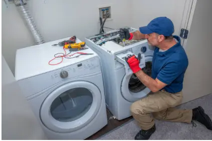 Technician testing a laundry appliance with a meter beside a washer and dryer