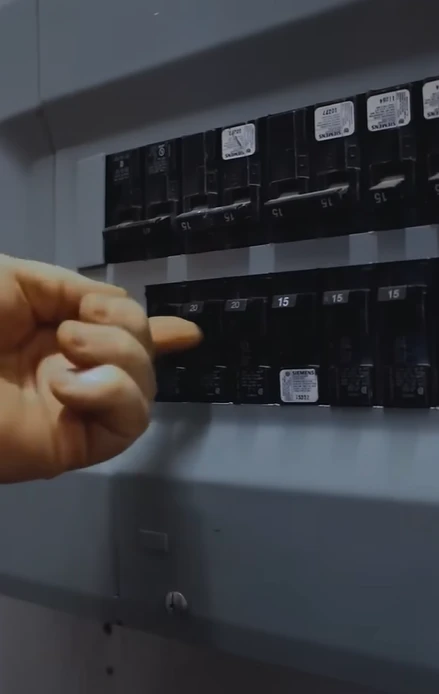 Hand pointing at circuit breakers in an electrical panel