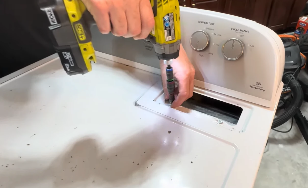 Technician drilling the screws out of the top of a white dryer